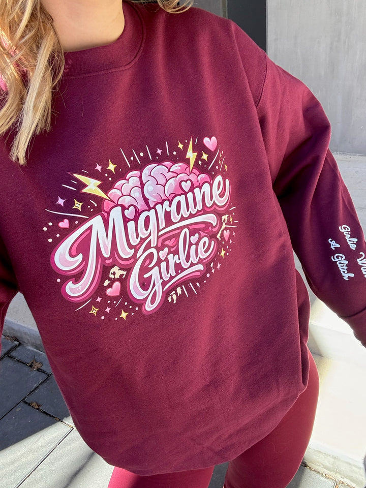 Maroon sweatshirt with 'Migraine Girlie' design worn by a person.