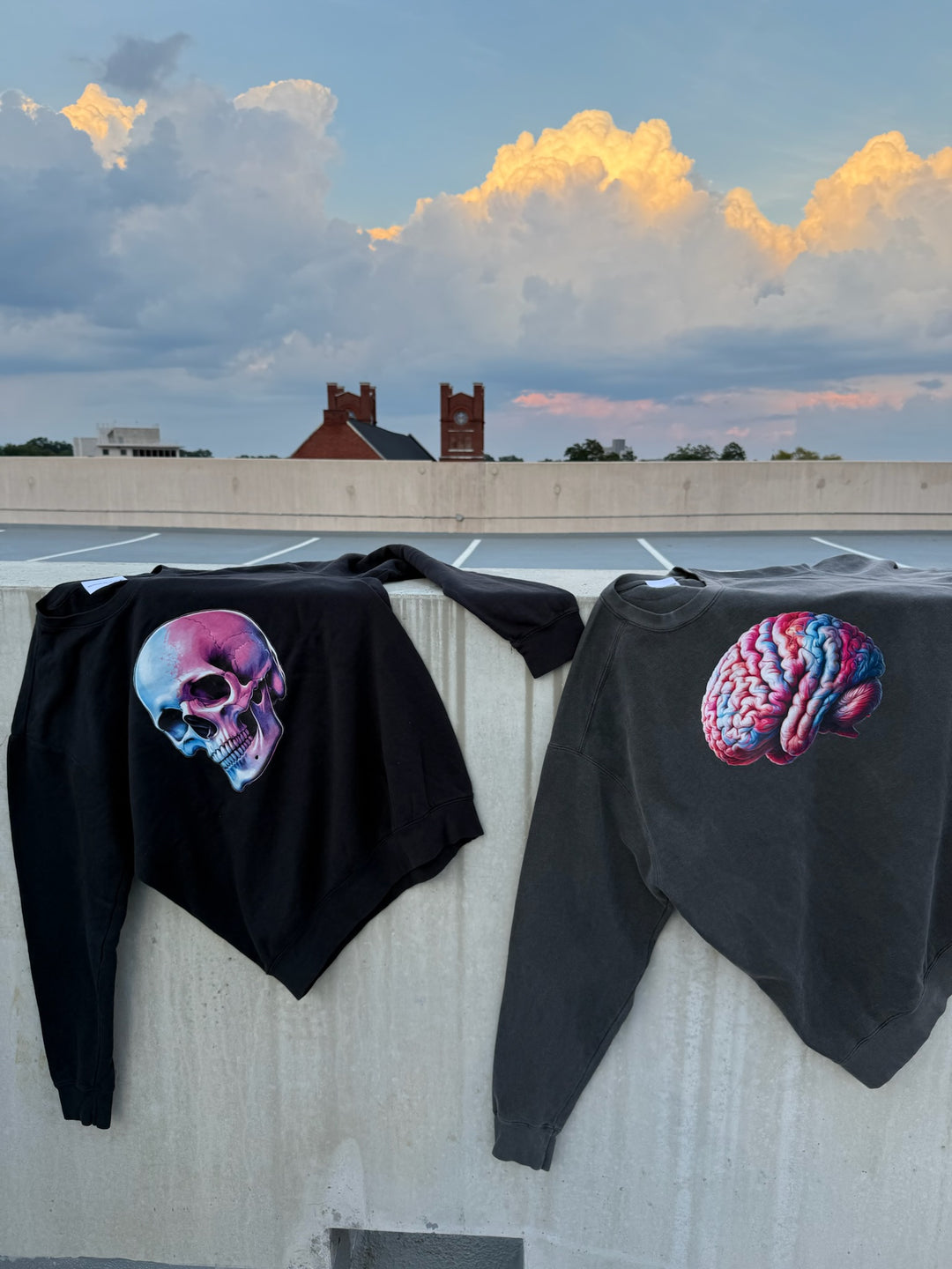 Two black sweatshirts on a concrete wall, one with a colorful skull, the other with a colorful brain