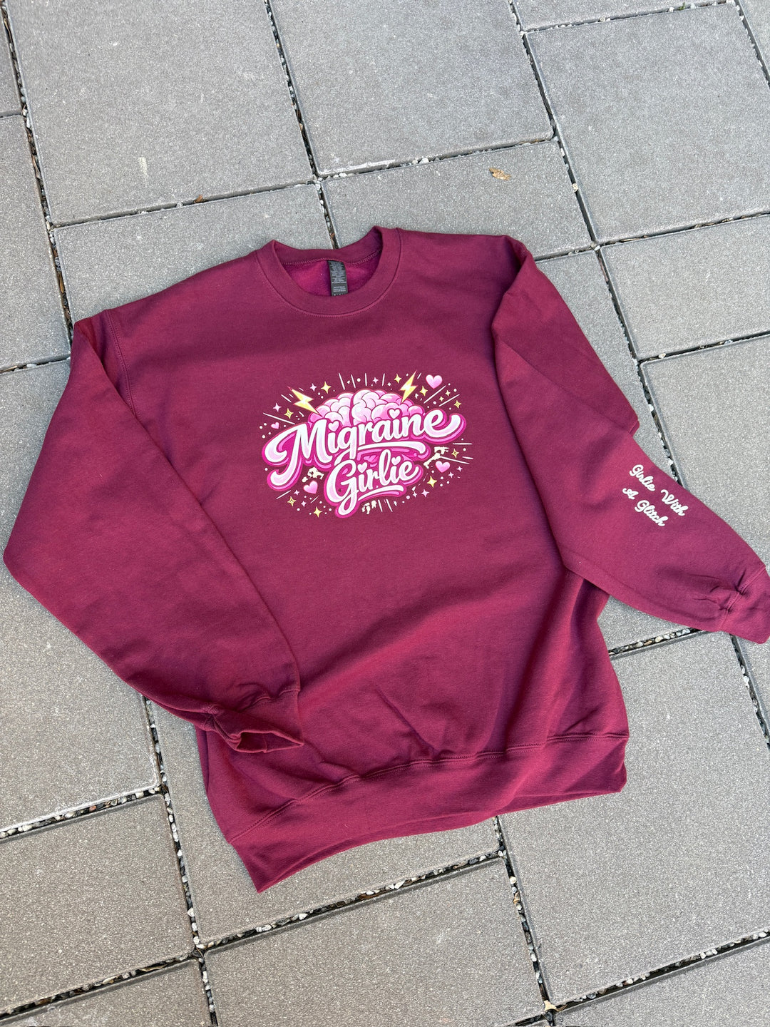 Maroon sweatshirt with 'Migraine Girlie' text on a tiled floor