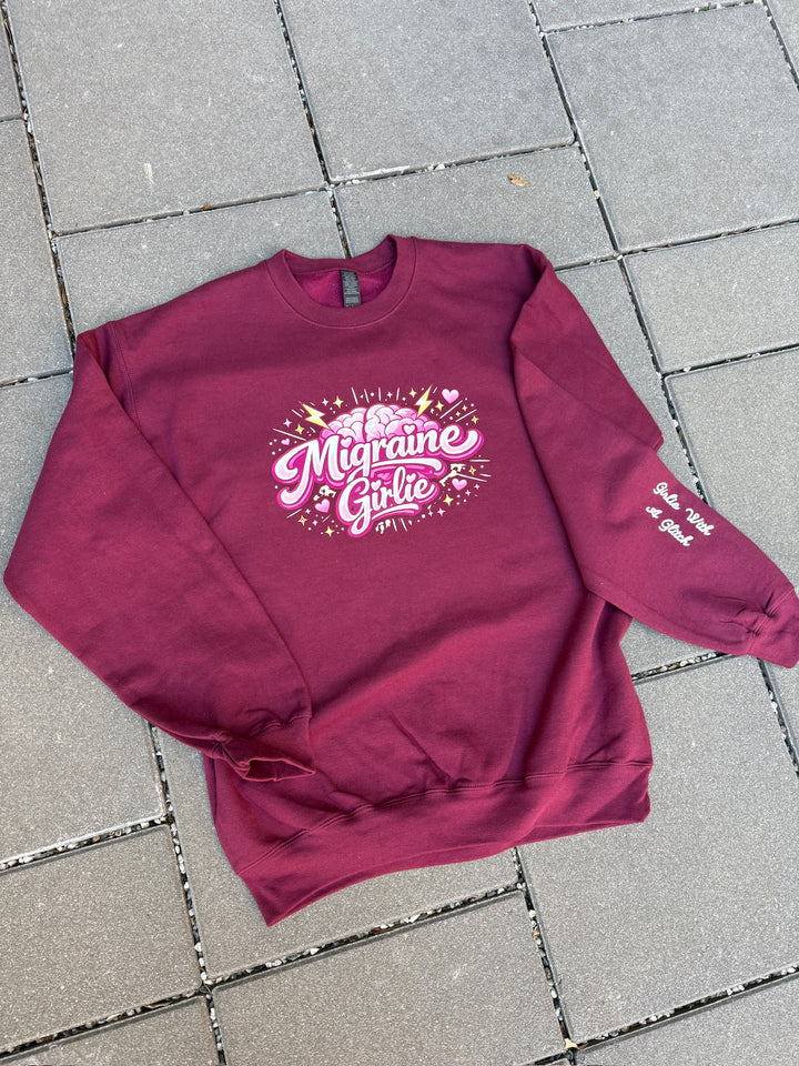 Maroon sweatshirt with 'Migraine Girlie' text on a tiled floor