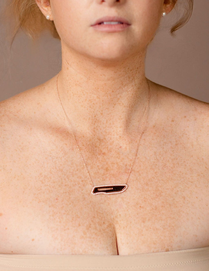 Close-up of a person wearing a diamond scalpel necklace on a neutral background