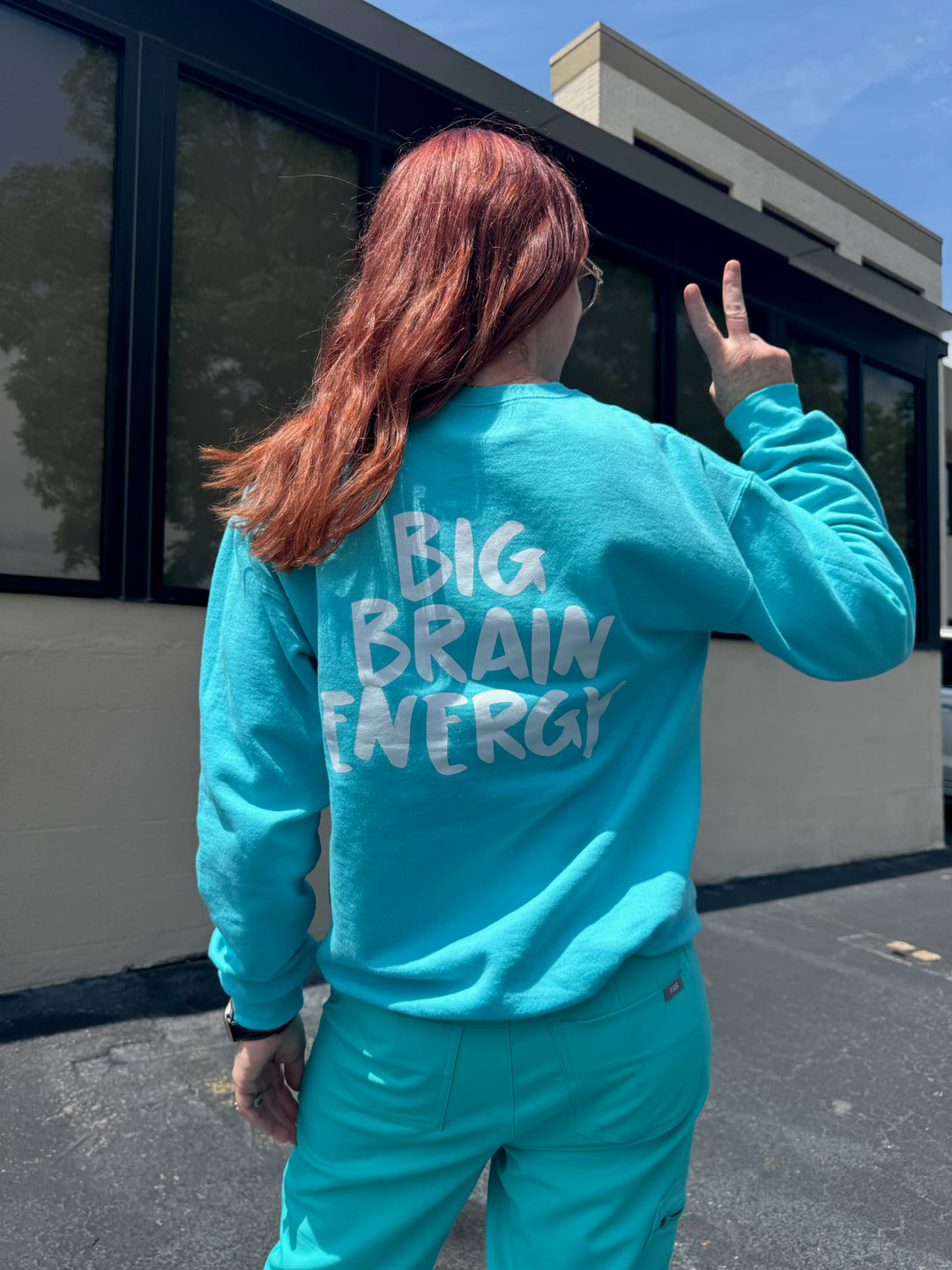 Ladyspinedoc giving the peace sign while wearing the Big Brain Energy Crewneck Sweatshirt – Seafoam showing the "BIG BRAIN ENERGY" catchphrase on the back