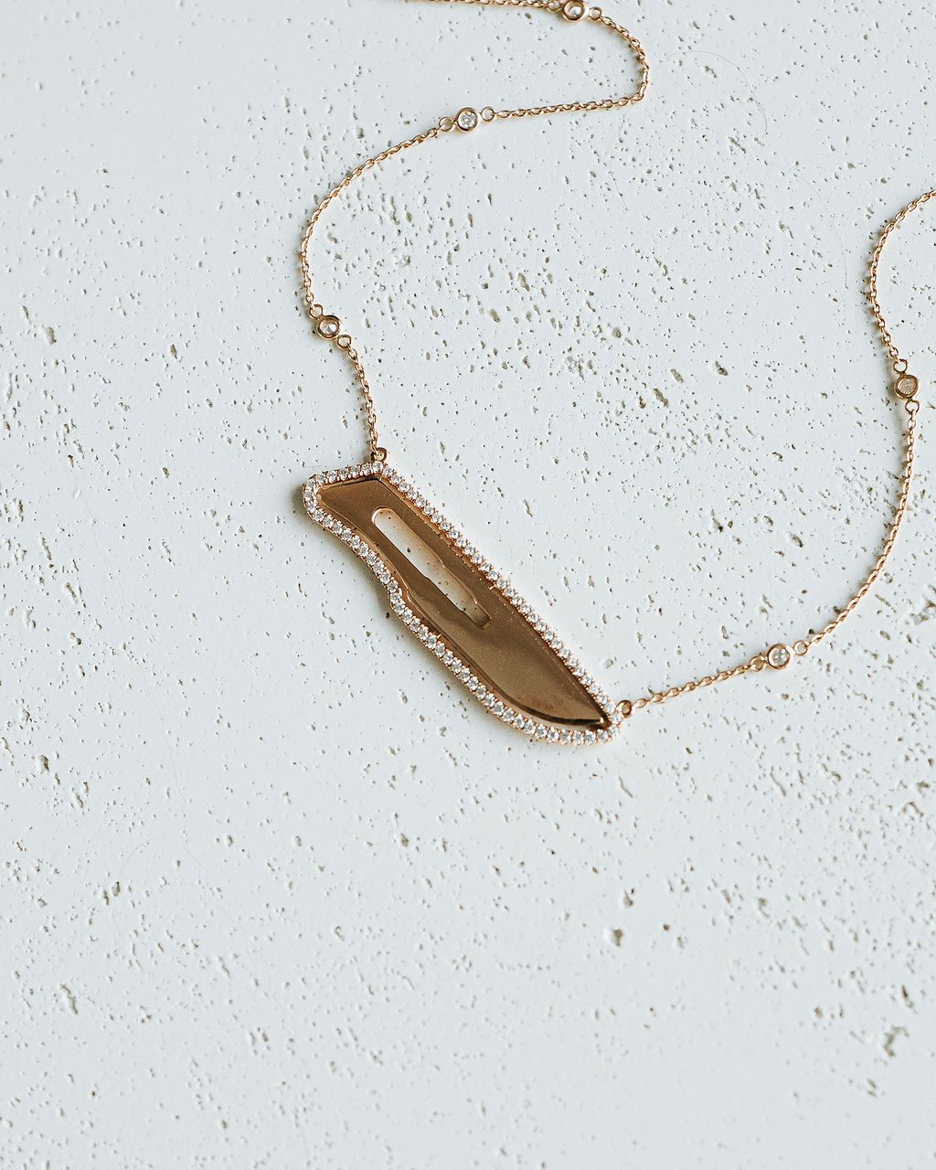 Necklace with a gold and diamond scalpel pendant on a light gray background