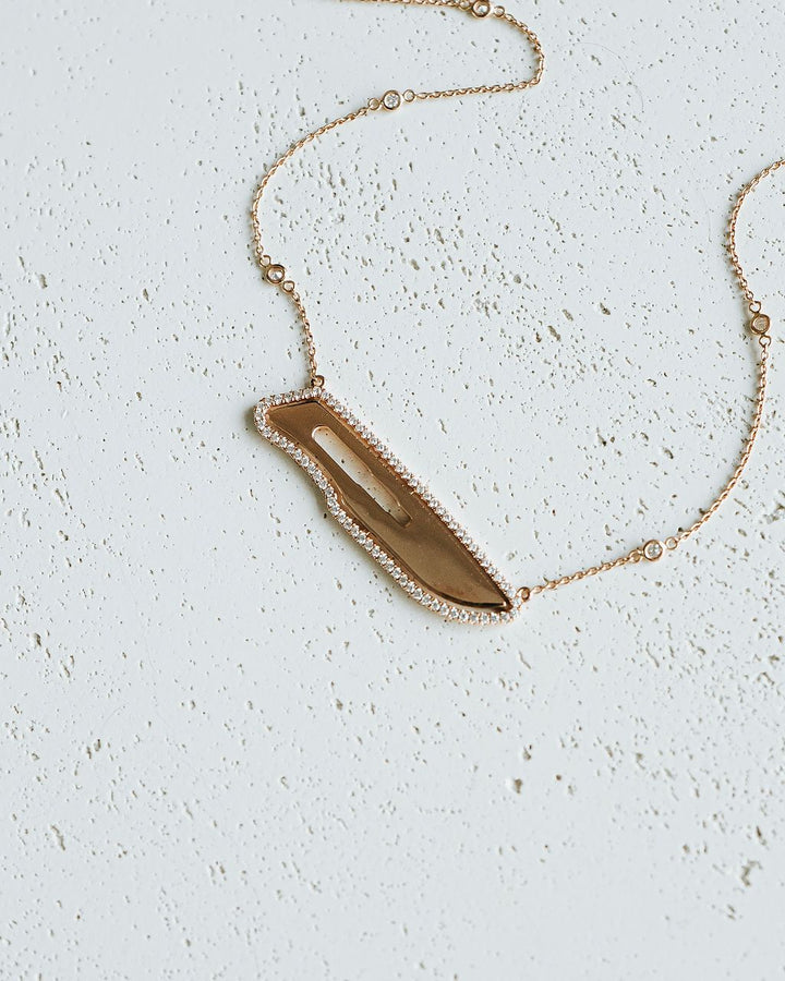 Necklace with a gold and diamond scalpel pendant on a light gray background