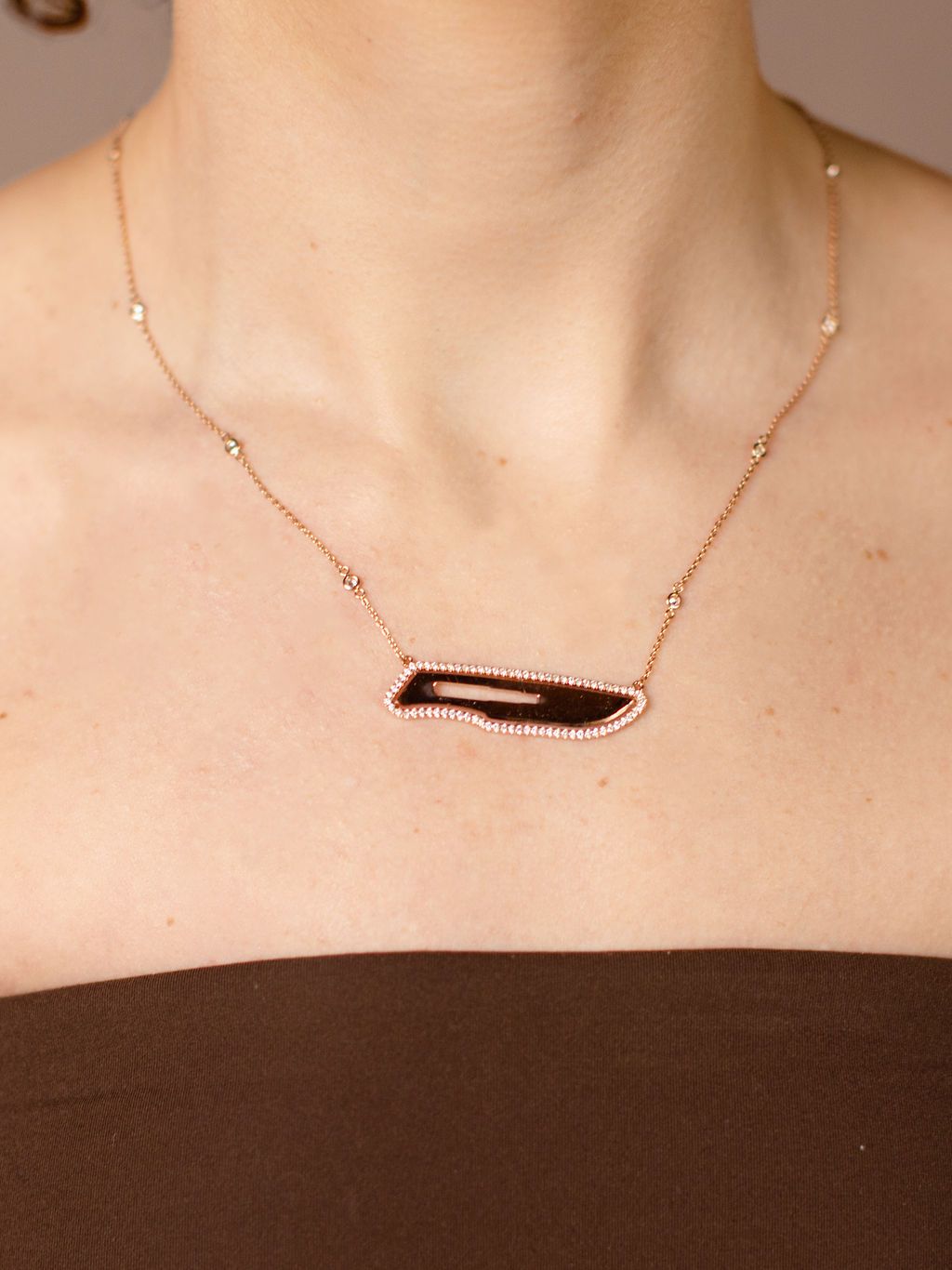 Necklace with a diamond scalpel pendant on a person wearing a brown top.