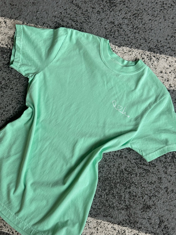 Flat lay of light green (Island Reef) Heart of Medicine t-shirt featuring stethoscope and heart waveform logo on the upper left chest.