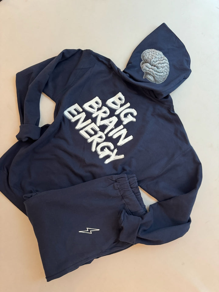 Back flat lay of navy hoodie showing the BIG BRAIN ENERGY print on the back and brain design on left side of hood. Folded BIG BRAIN ENERGY sweatpants with lightning bolt logo also shown.
