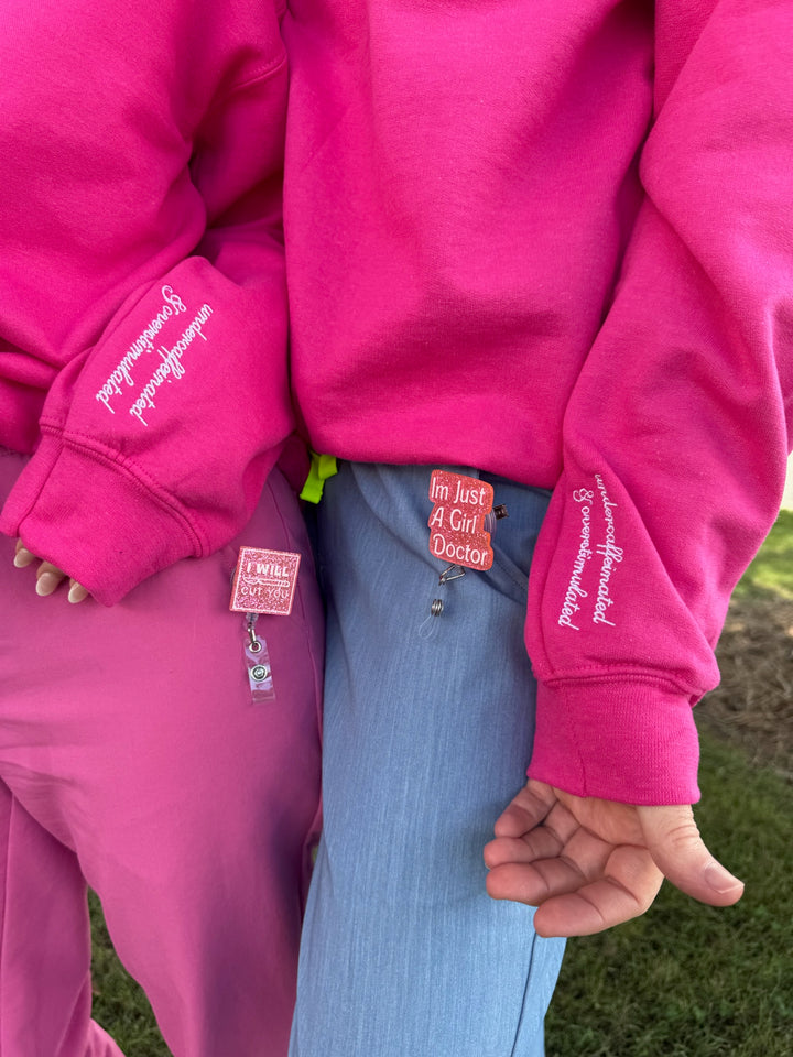 Person wearing a bright pink outfit with undercaffeinated and overstimulated text on sleeves, standing outdoors.