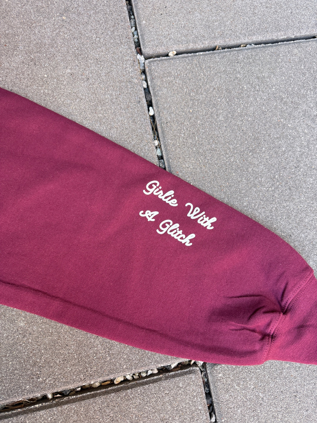 Maroon sleeve with 'Girlie With A Glitch' text on a gray pavement background