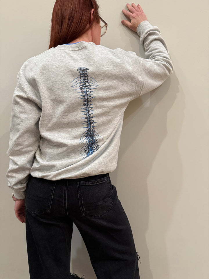 A person wearing a gray long sleeve tee with a spine graphic on the back, paired with black jeans.
