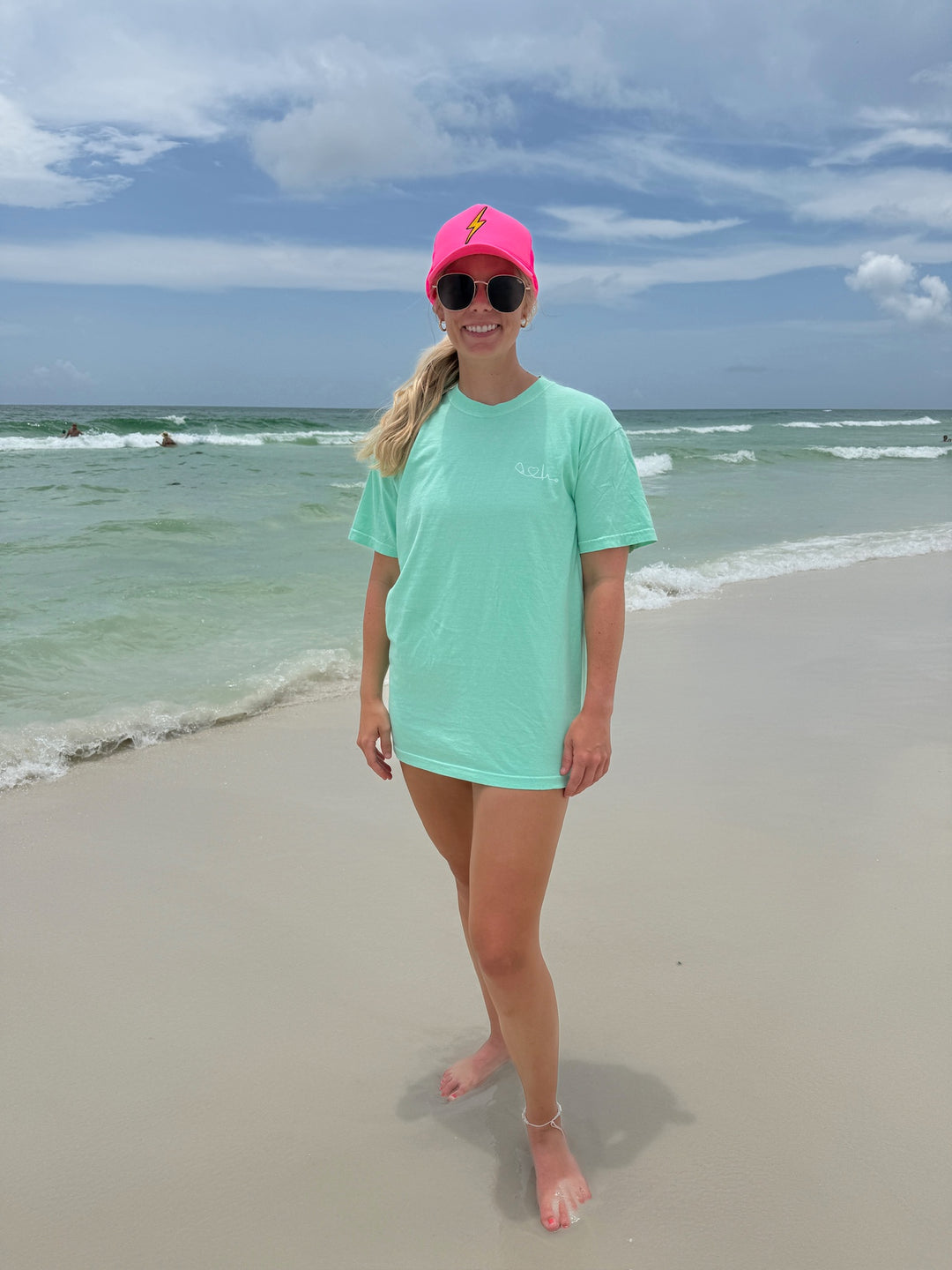 Woman at beach wearing the Island Reef light green Heart of Medicine t-shirt featuring stethoscope and heart waveform logo on the upper left chest.