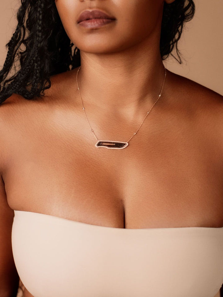 Close-up of a person wearing a scalpel necklace with a neutral background