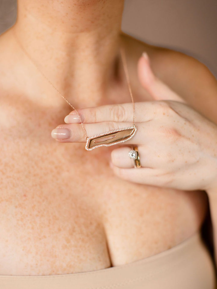 Person wearing a rose gold and diamond scalpel necklace, set against a neutral background.