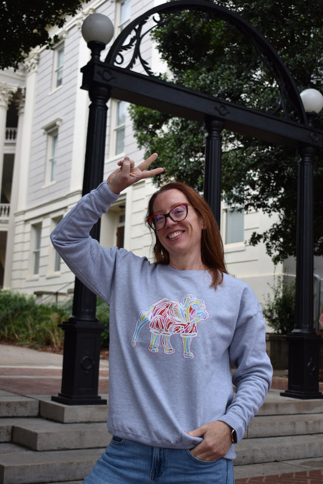 Person wearing a light gray sweatshirt with a colorful bulldog design, standing outdoors.