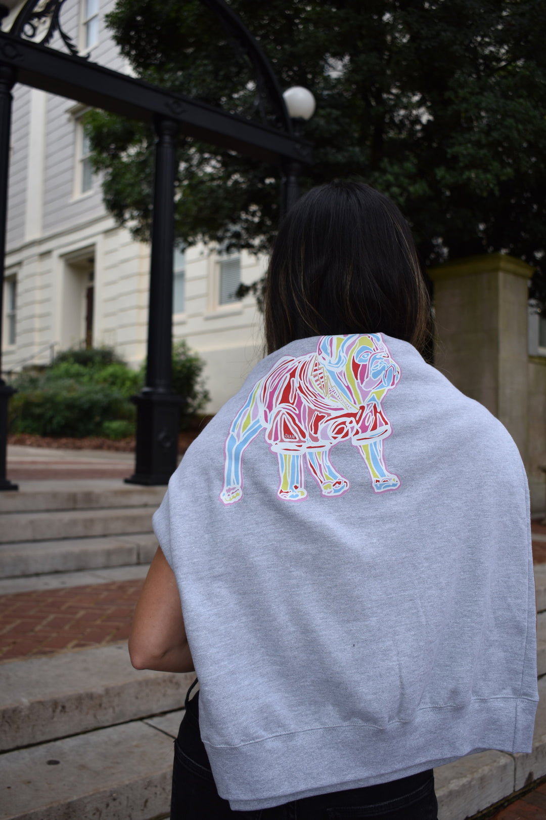 Person wearing a gray sweatshirt with a colorful bulldog design on the back, standing outdoors.