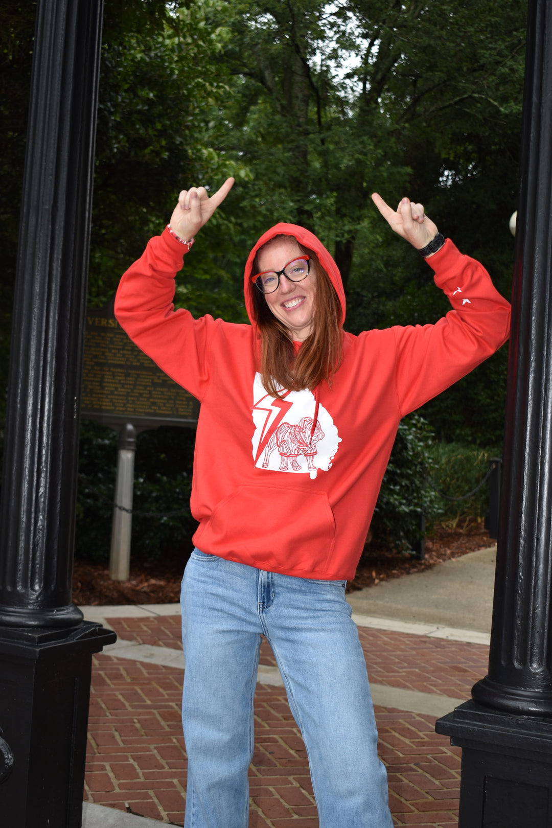 Person wearing a red hoodie with a bulldog graphic design, standing outdoors with trees and a path in the background.