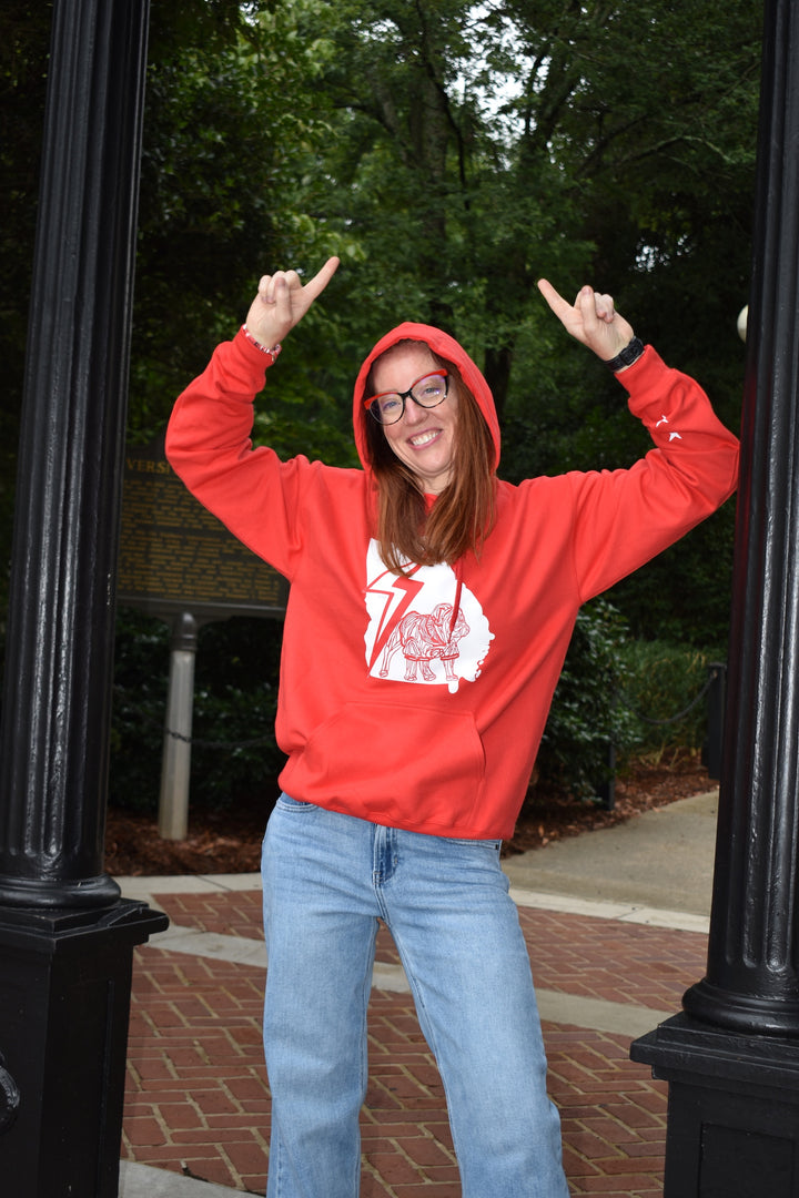 Person wearing a red hoodie with a bulldog graphic design, standing outdoors with trees and a path in the background.