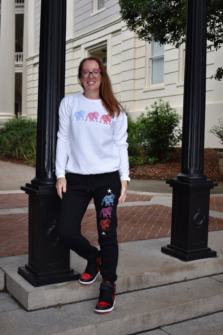 Person wearing a white sweatshirt and black pants with colorful designs, standing outdoors.