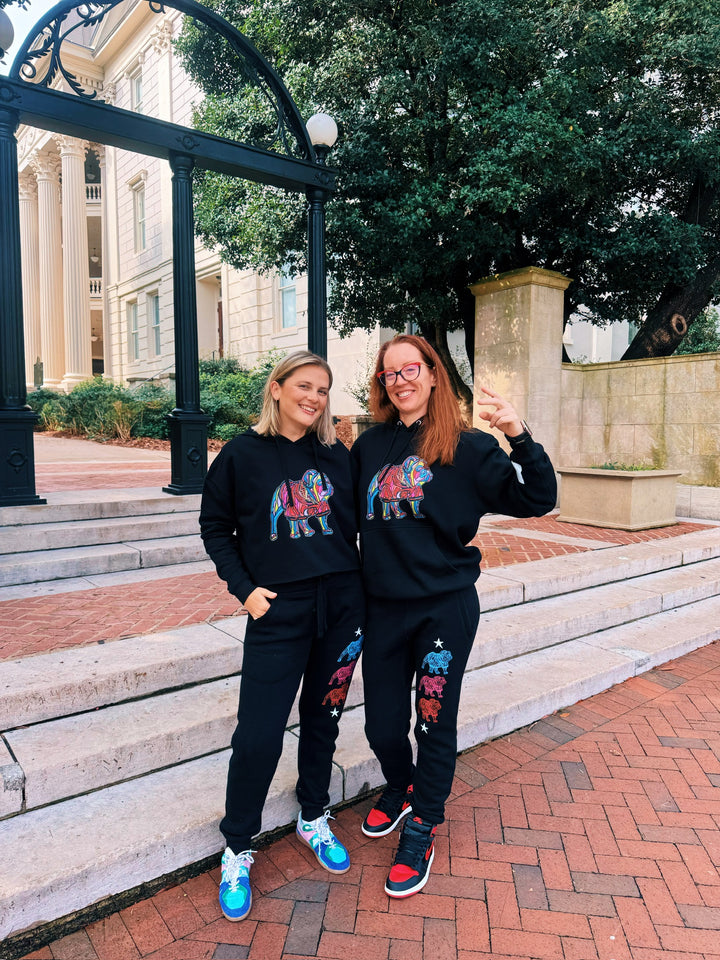 Two people wearing matching black sweatshirts with colorful bulldog designs in front of a building.