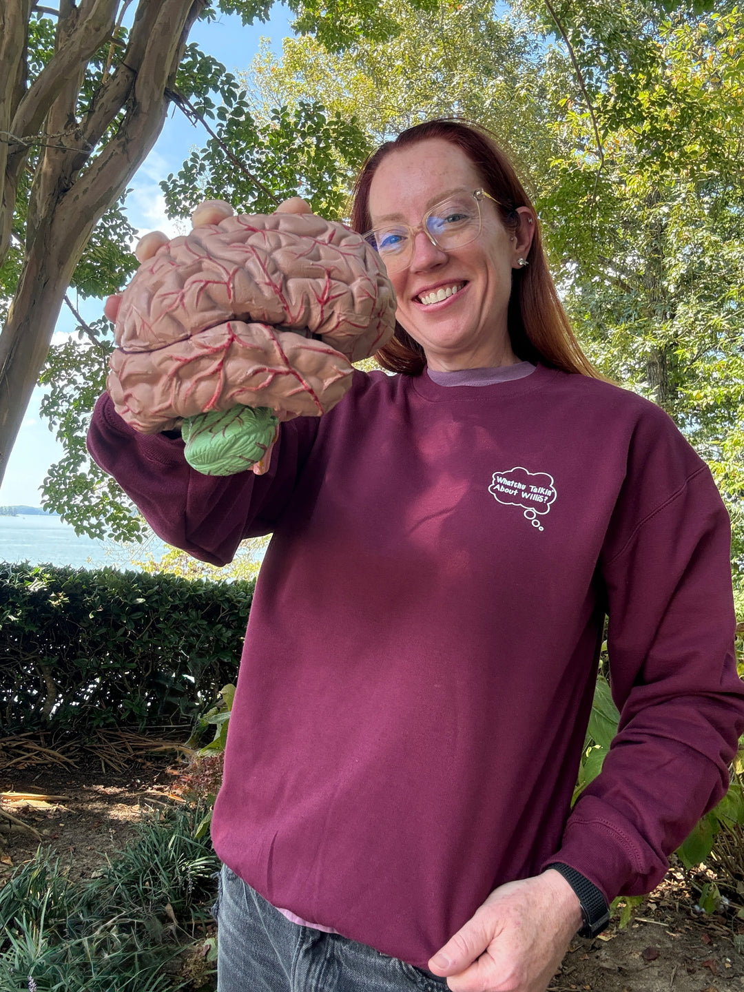 Ladyspinedoc wearing a Whatchu Talkin’ About Willis Sweatshirt and holding a model of a brain outdoors with trees in the background