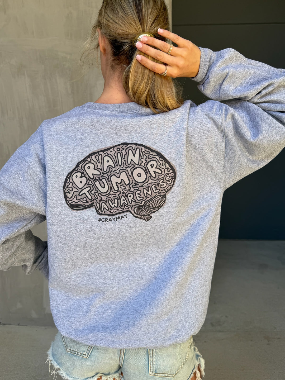 Person wearing a gray sweatshirt with 'Brain Tumor Awareness' design on the back.