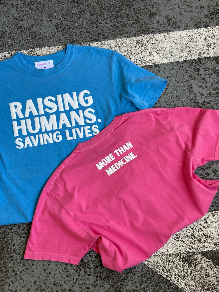 Blue and pink Raising Humans Saving Lives t-shirts with text on a textured surface