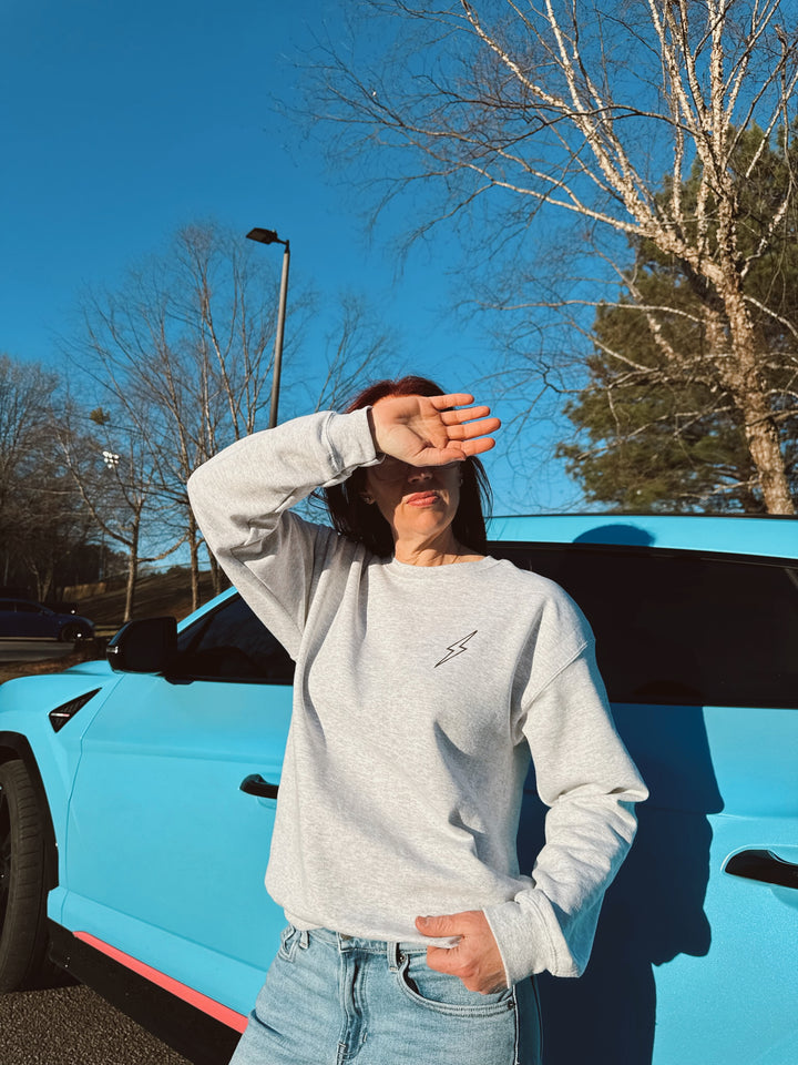 Ladyspinedoc wearing a gray crewneck sweatshirt standing next to a blue vehicle.