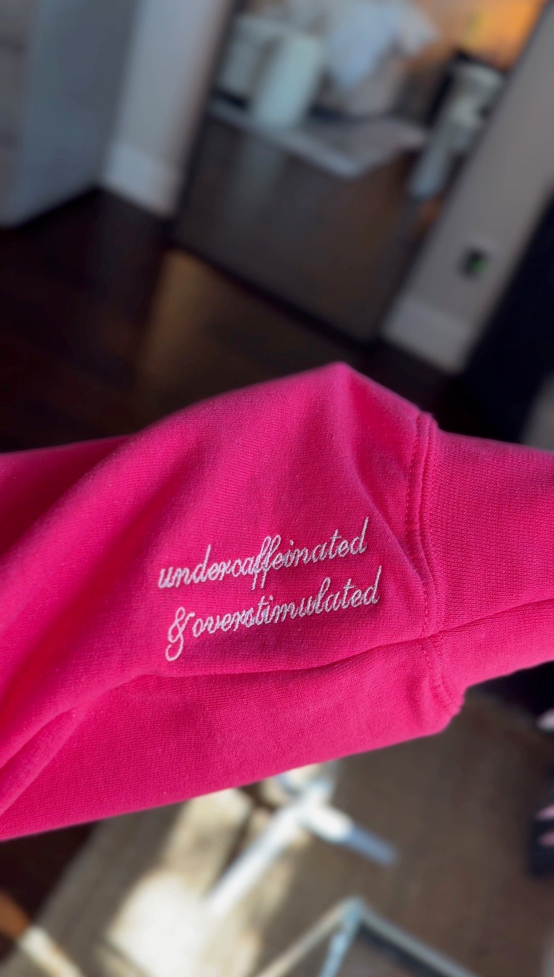 Pink shirt with text 'undercaffeinated & overstimulated' on a blurred background