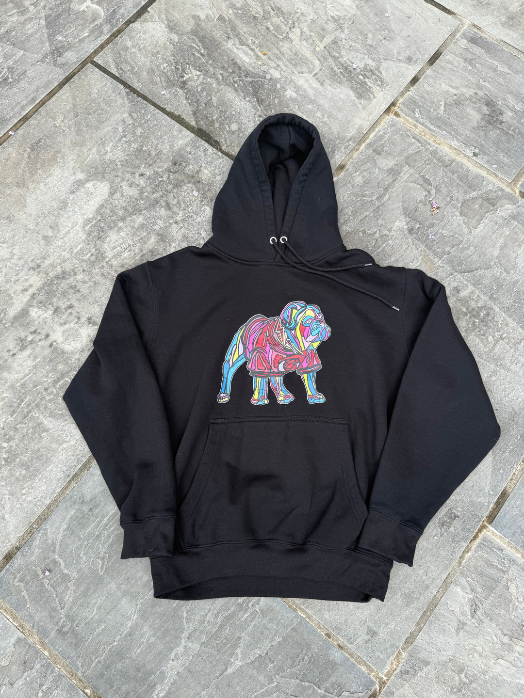 Black hoodie with a colorful bulldog design on a stone pavement