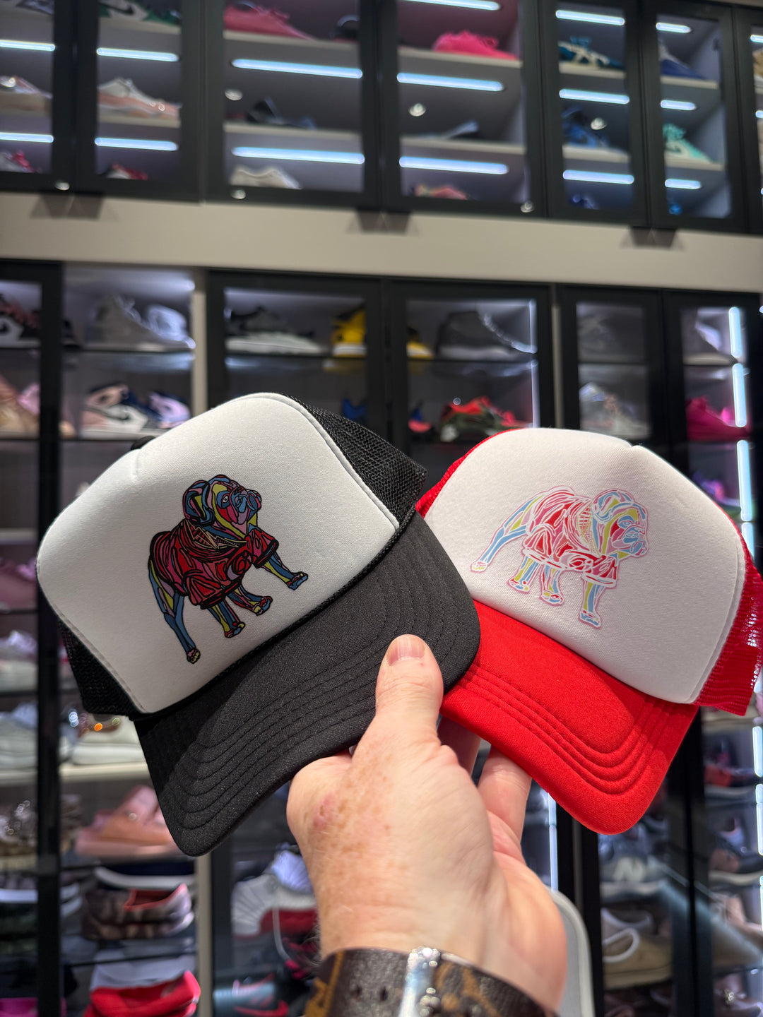 Two Chan Art Collab hats with colorful designs held in front of a shoe display.