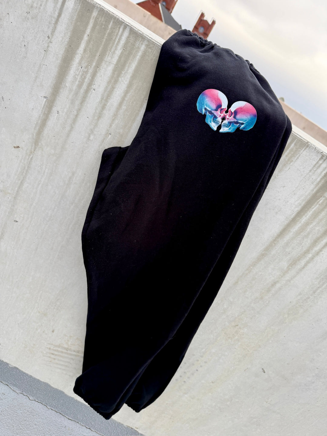 Super Skull Sweatpants - Black Joggers with Skull Design laying on a concrete wall
