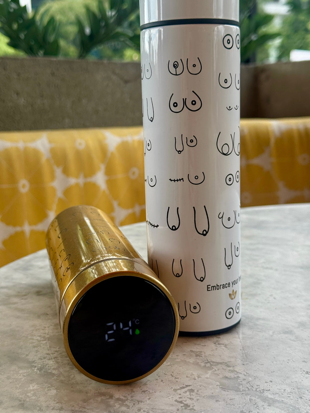 White Smart Water Bottle standing up on table and LED Temperature Display shown on gold version laying on its side