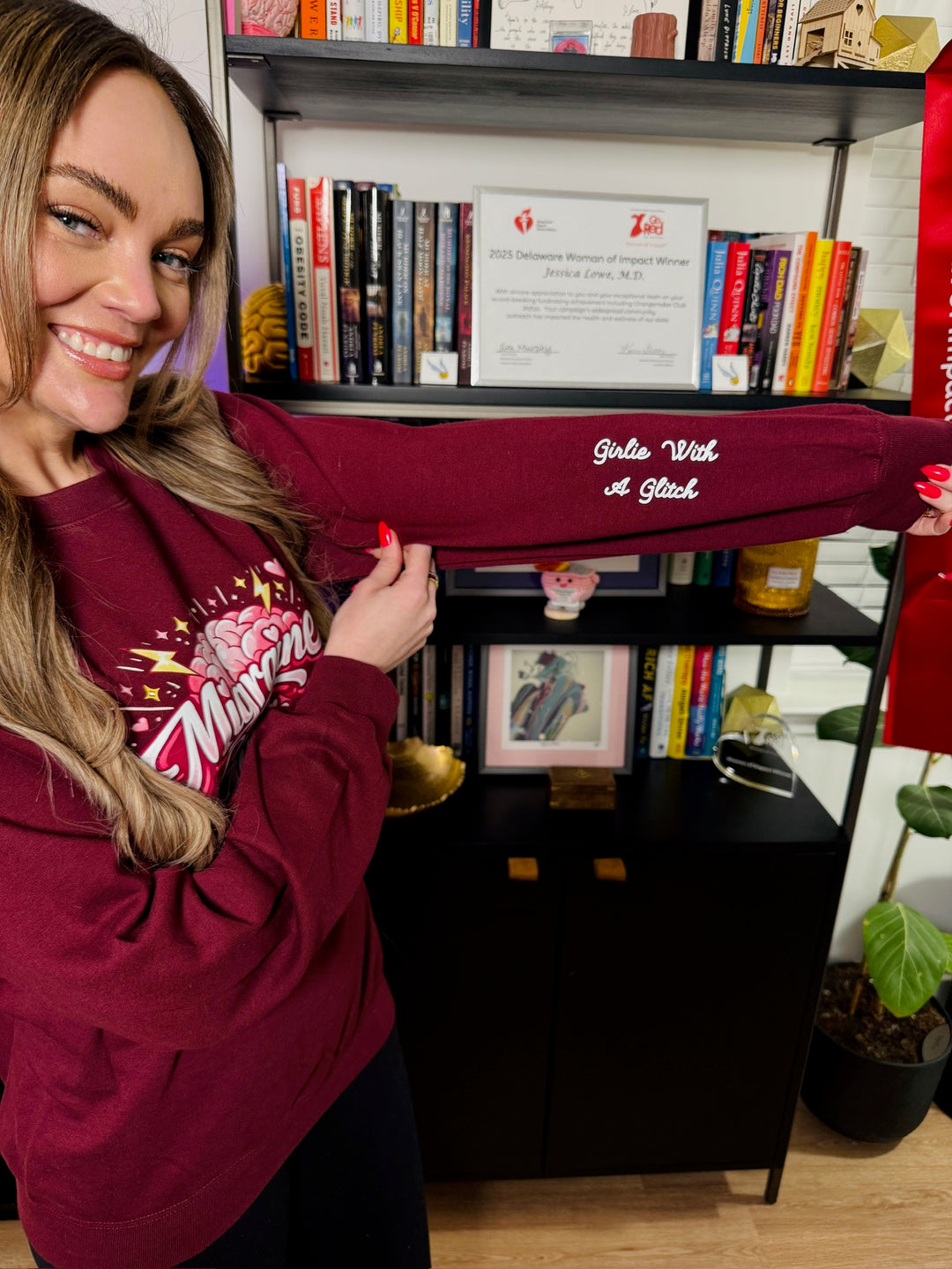 Dr. Brain Barbie wearing a burgundy Migraine Girlie sweatshirt and showing off the Girlie with a Glitch Sleeve art