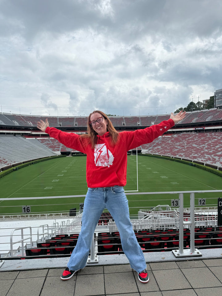 Person wearing a red sweatshirt with a logo in front of a large stadium
