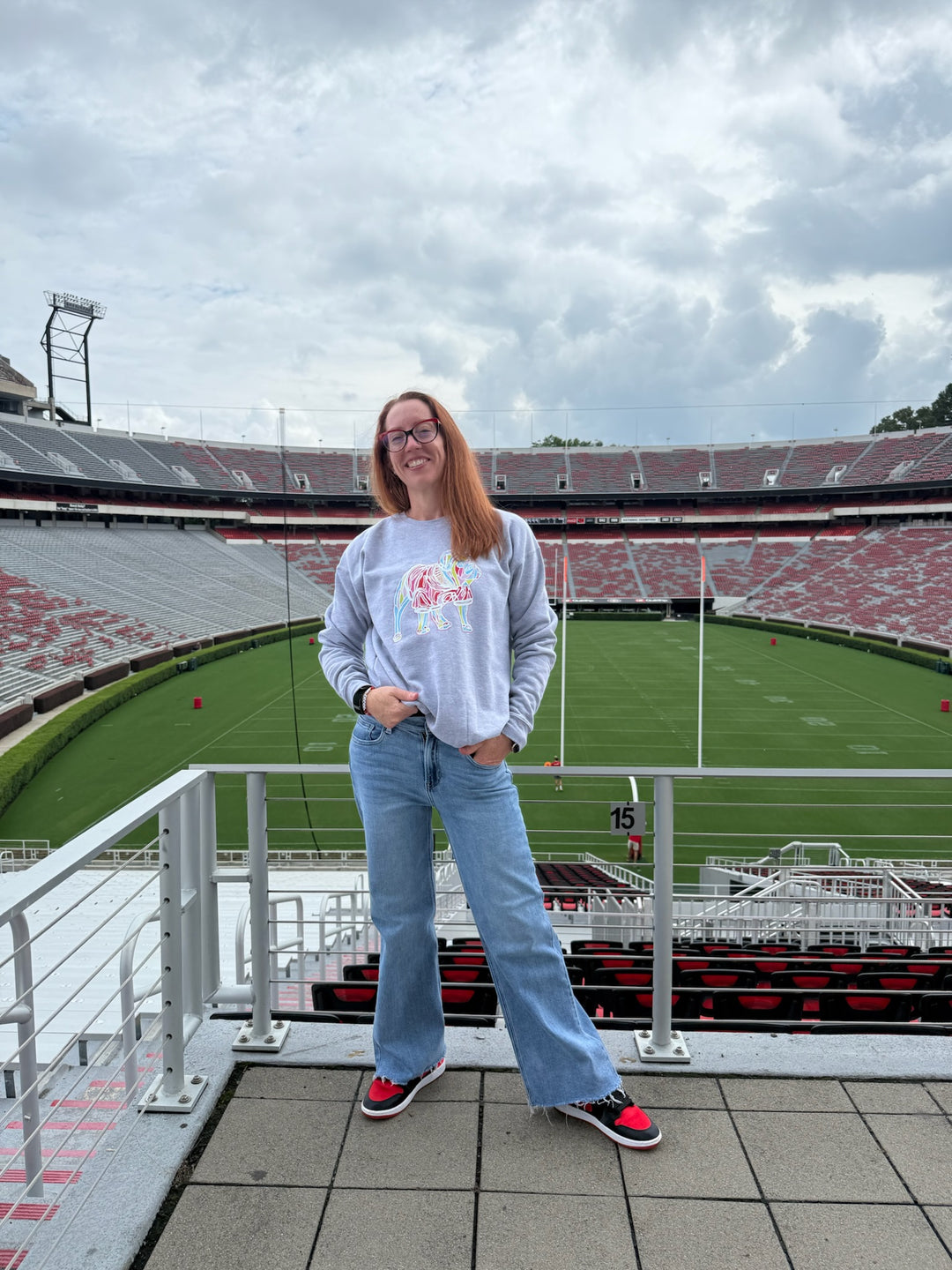 Person standing on a raised platform overlooking a football stadium with a cloudy sky.