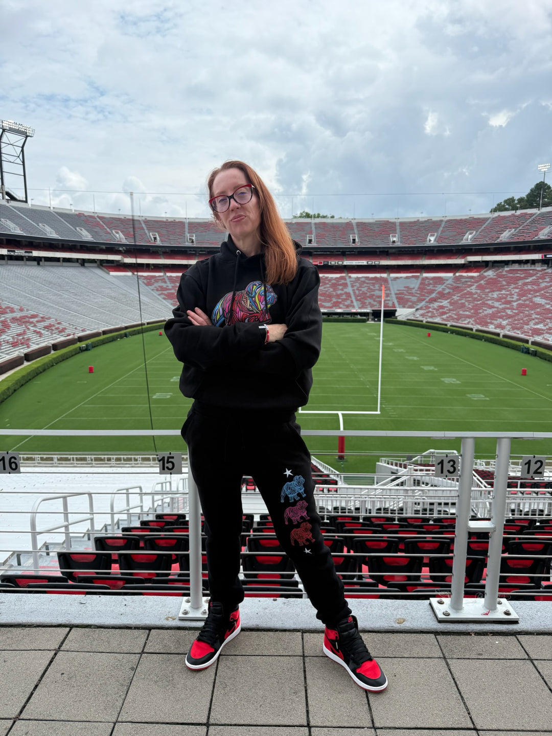 Ladyspinedoc in bulldog gear standing in front of a large stadium with green field and red seats.