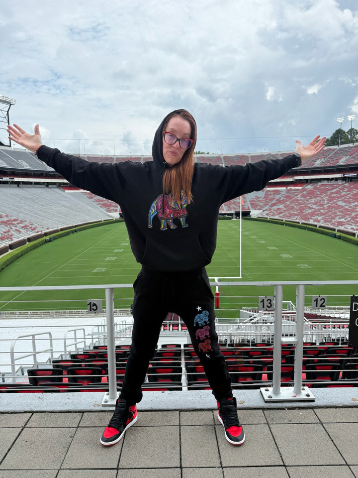 Person in black bulldog hoodie and pants standing in front of a stadium with open arms