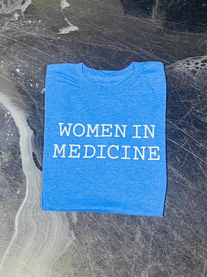 Blue t-shirt with 'WOMEN IN MEDICINE' text on a textured surface