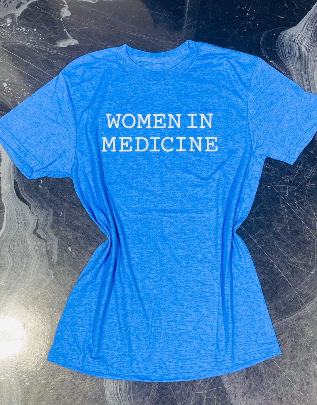 Blue t-shirt with 'WOMEN IN MEDICINE' text on a reflective surface