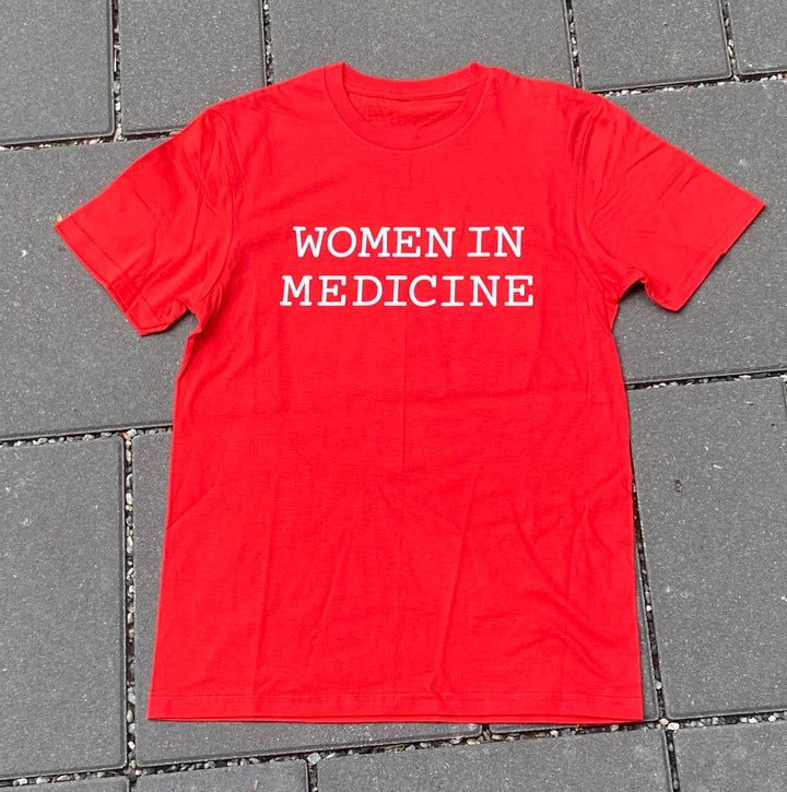 Red t-shirt with 'WOMEN IN MEDICINE' text on a gray tiled floor.