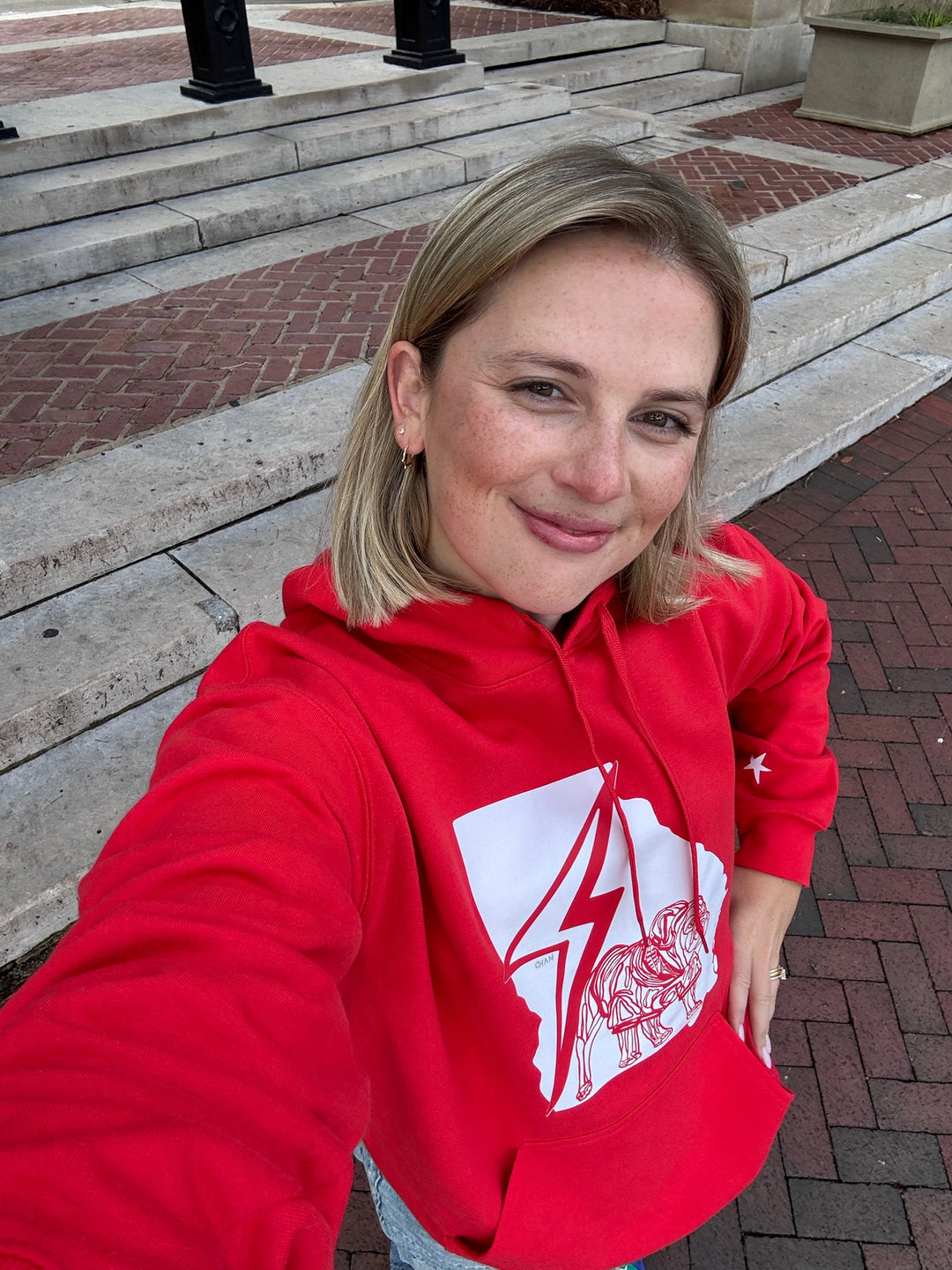 Woman wearing a red hoodie with a graphic design outdoors on a paved area.