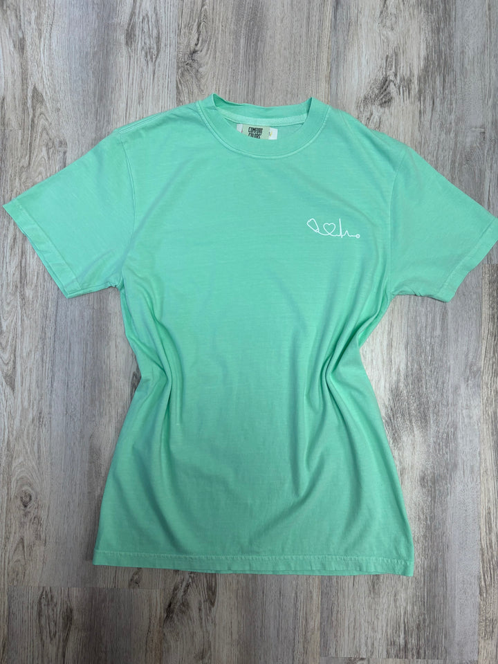 Front view of light green Heart of Medicine t-shirt featuring stethoscope and heart waveform logo on the upper left chest.