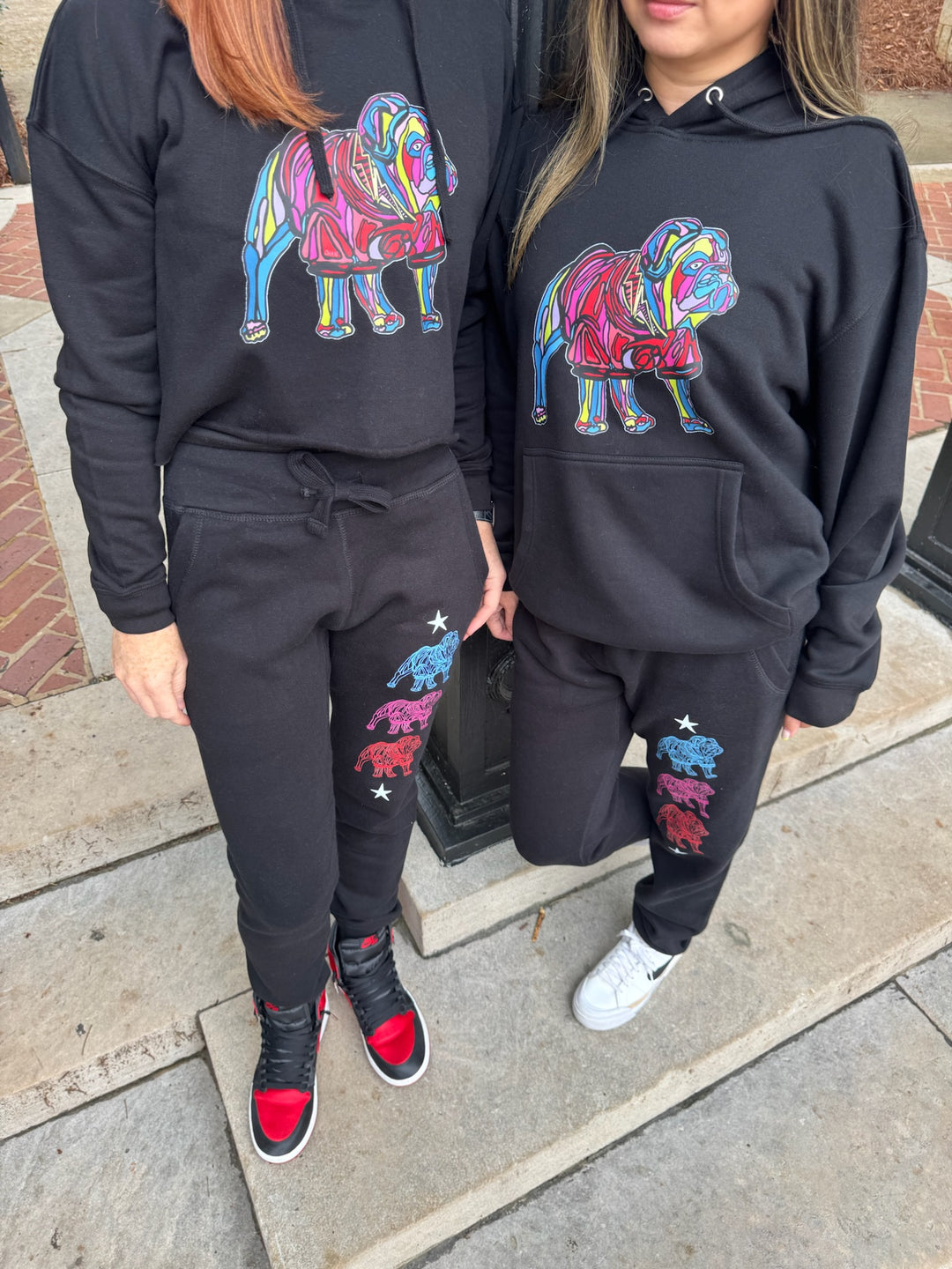 Two people wearing matching black hoodies and pants with colorful e bulldog designs.