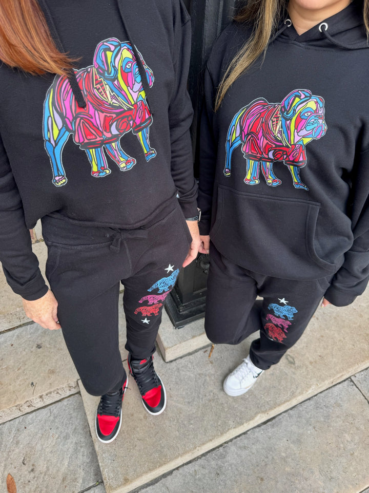 Two people wearing matching black hoodies with colorful bulldog designs on a sidewalk.