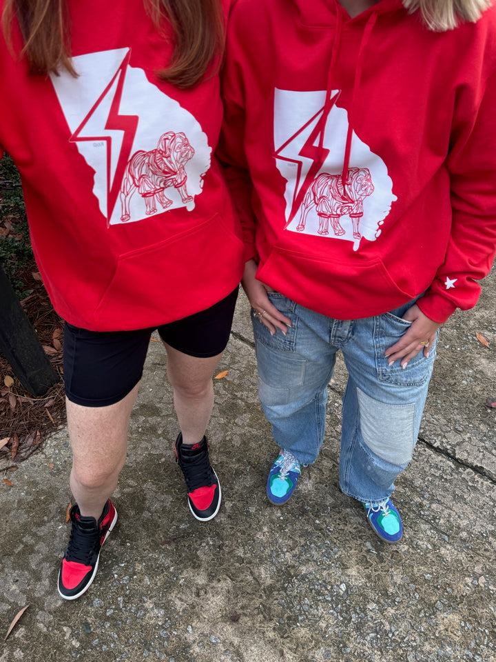 Two people wearing red hoodies with a white bulldog graphic design on a concrete surface.