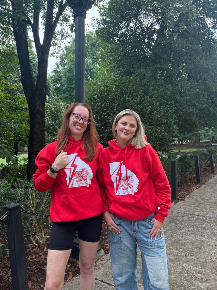 Two people wearing red hoodies with a bulldog logo in an outdoor setting.