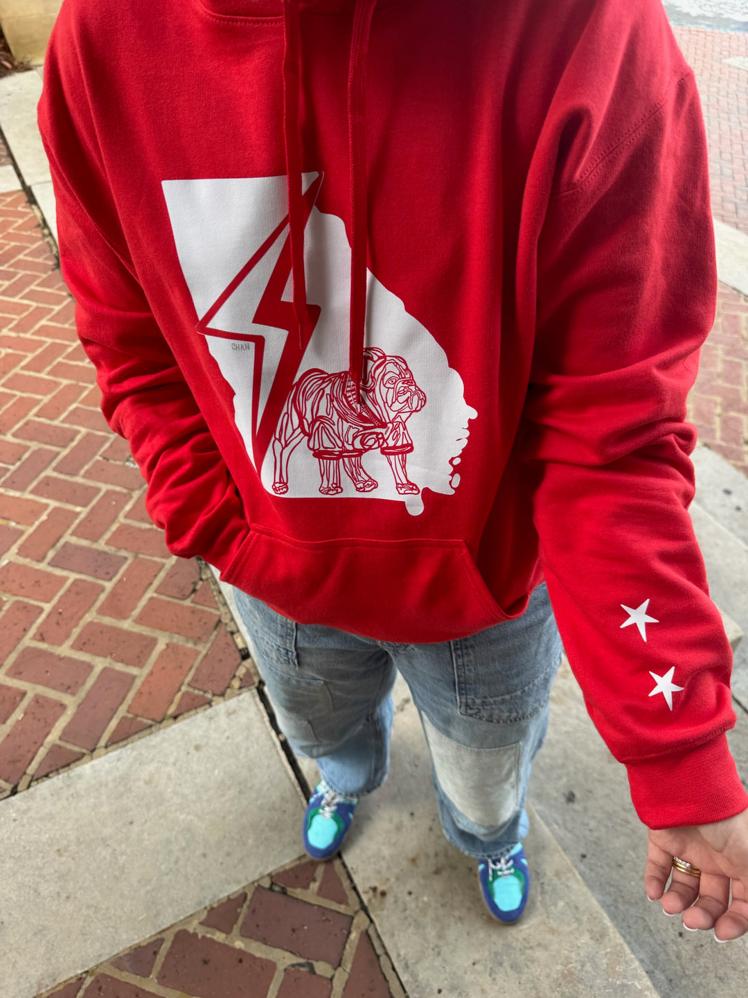 Person wearing a red hoodie with a white bulldog graphic design on a sidewalk.
