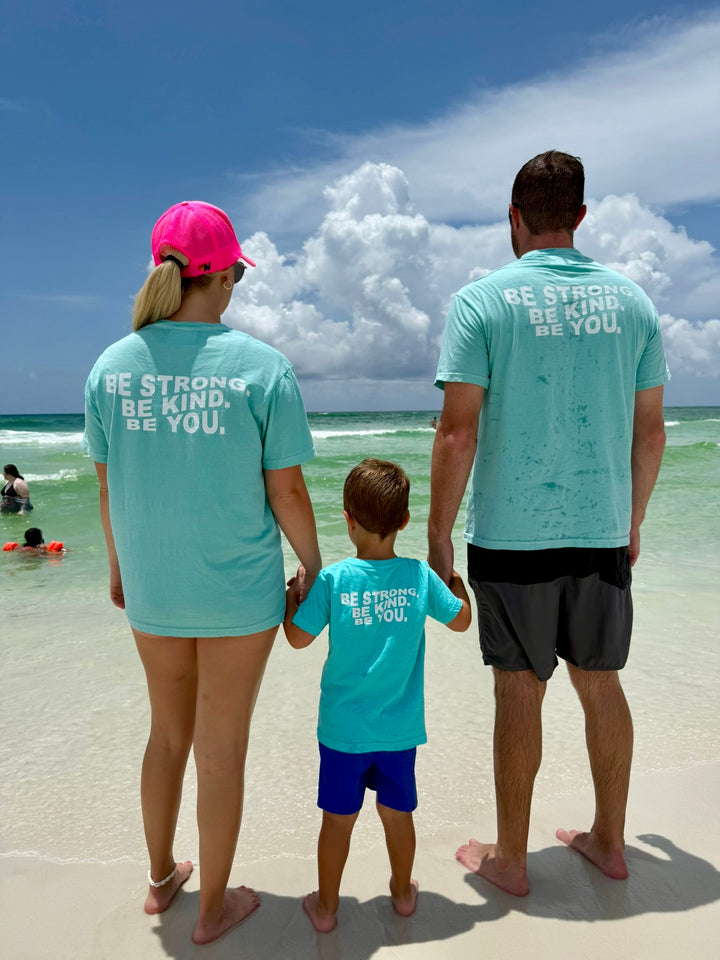 Mom and dad at beach with their toddler wearing the Be You Toddler Tee - Kids Caribbean Blue T-Shirt with Motivational “BE STRONG. BE KIND. BE YOU.” Motto