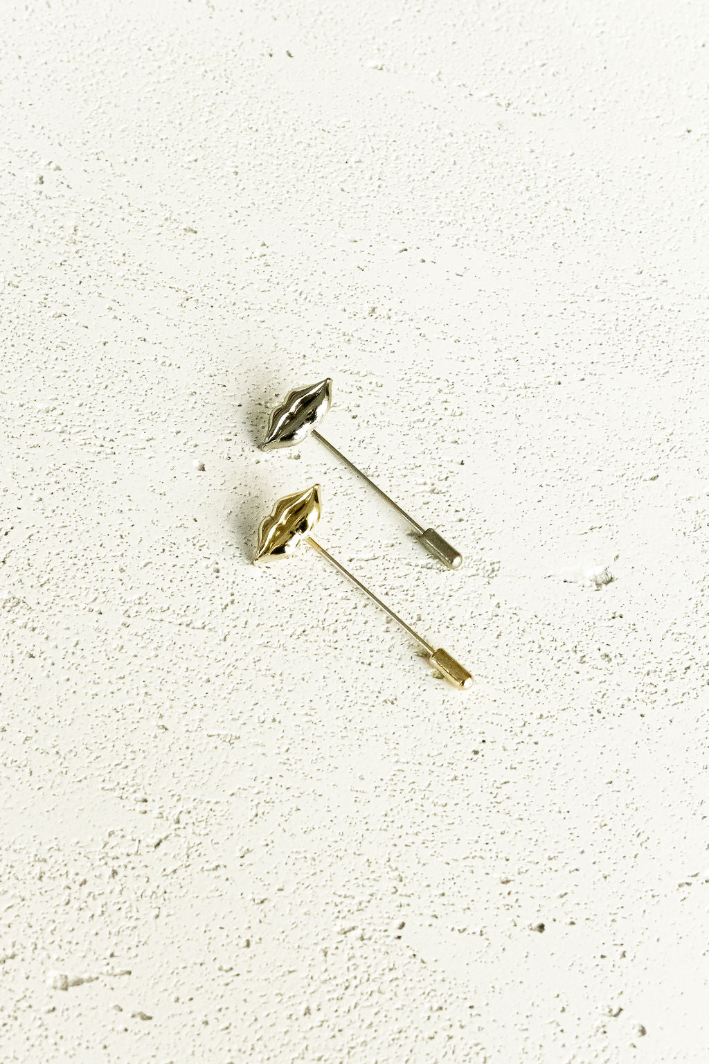 Two lips stick pins, one gold, the other silver