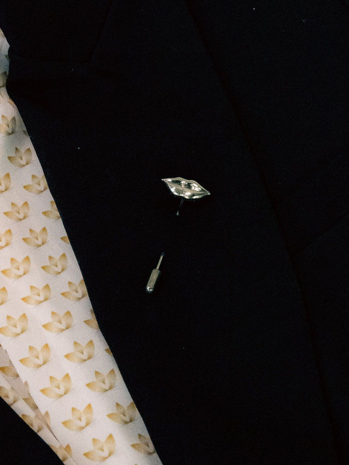 Close-up of a black garment with a decorative lip lapel pin on a patterned fabric background
